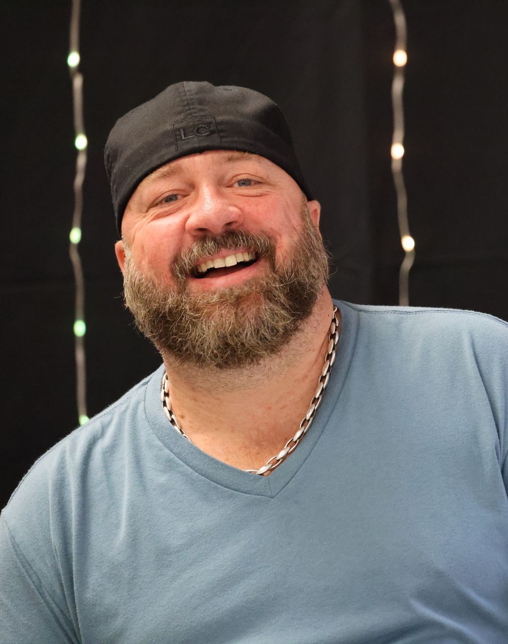 A man with a beard wearing a blue shirt and a black hat