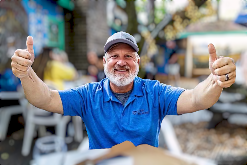 A man in a blue shirt is giving a thumbs up.