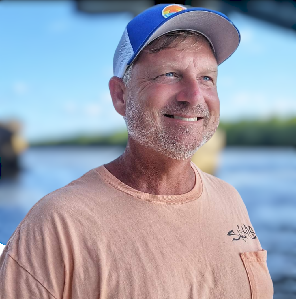 A man wearing a hat and a peach shirt is smiling