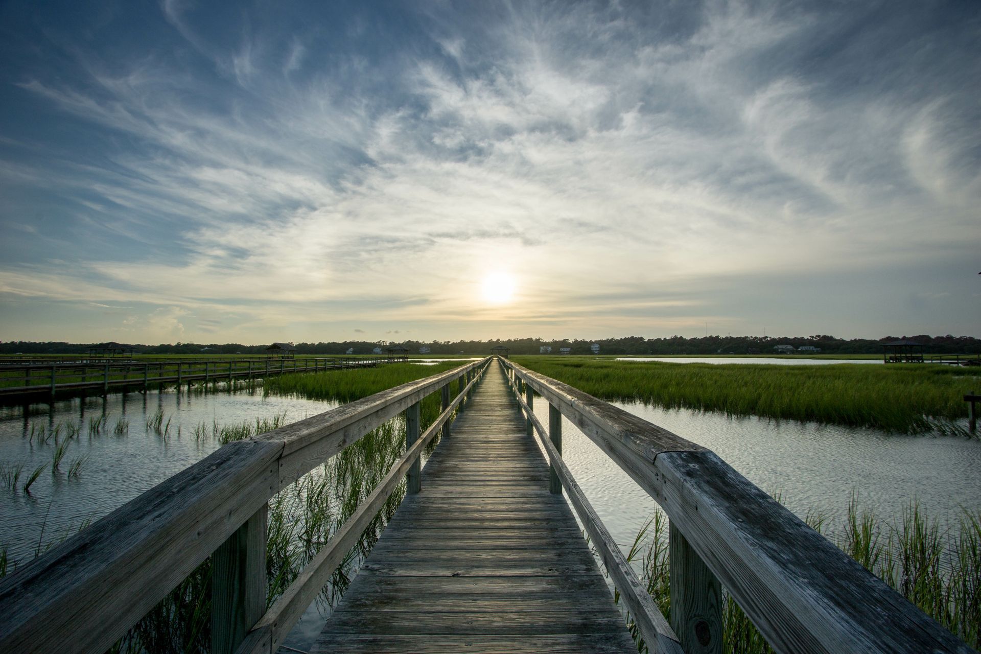 A wooden bridge over a body of water with the sun shining through the clouds.