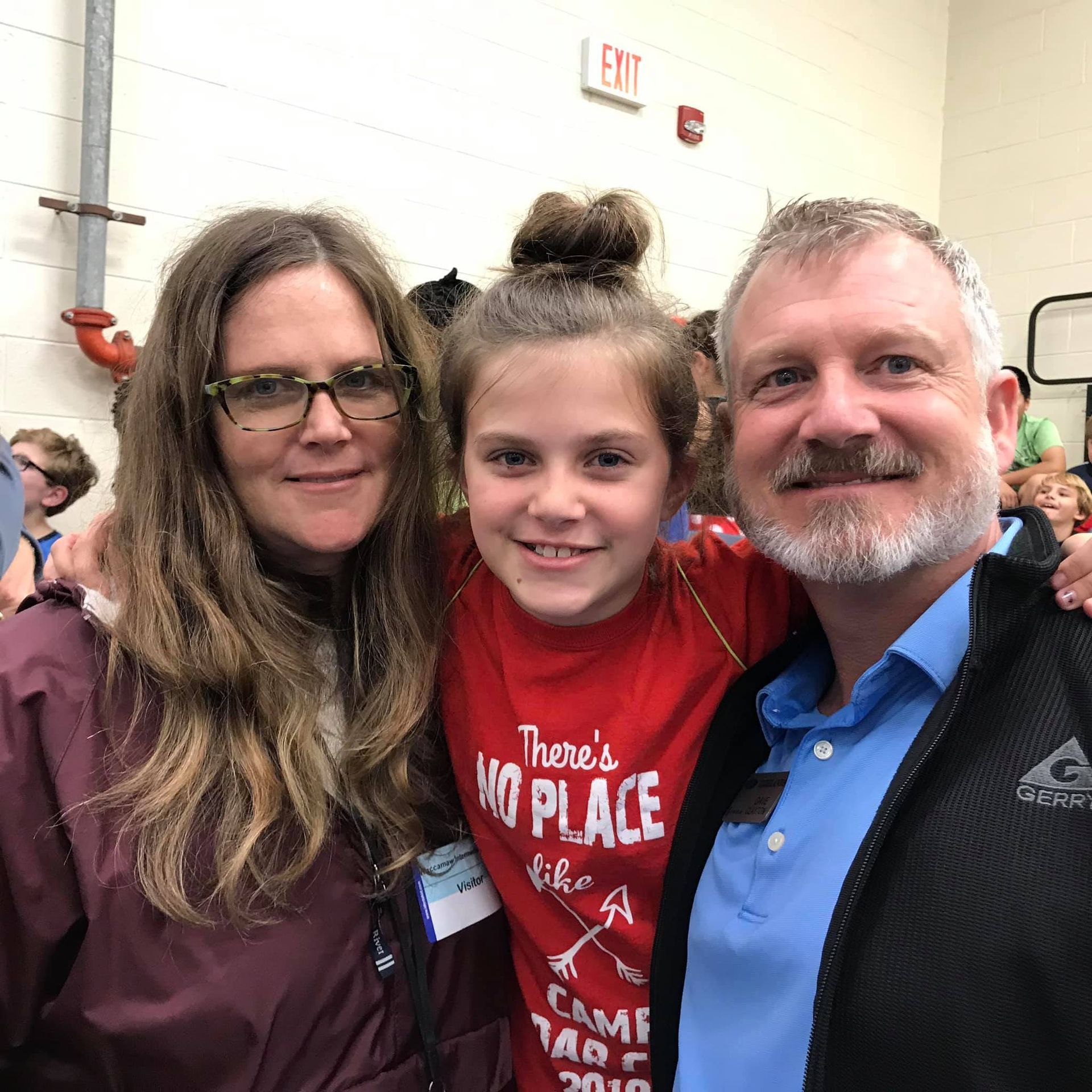A man and woman are posing for a picture with a young girl wearing a red shirt that says there 's no place like home