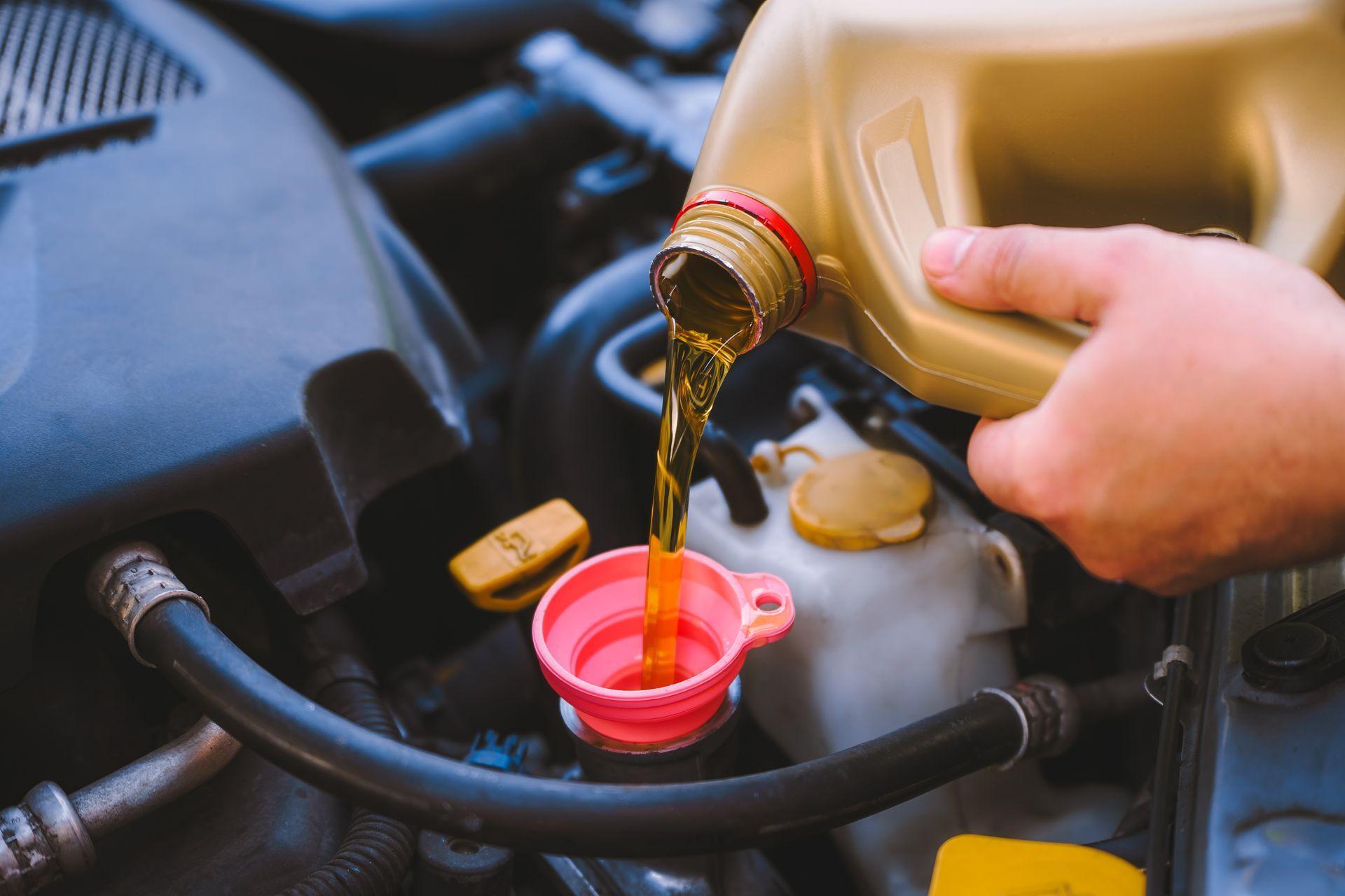 A person pouring golden motor oil from a plastic jug into a car engine using a pink funnel.