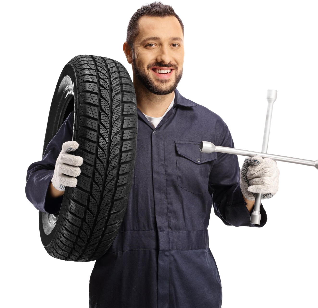 A smiling technician in dark blue coveralls and gloves holding a car tire in one hand and a lug wrench in the other.