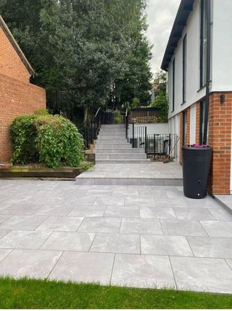A patio with grey stone paving leading to wide, tiered steps rising toward a landscaped garden area between two buildings.