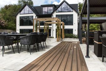 A modern white house with a patio featuring a wooden walkway, outdoor dining furniture, and a pergola.