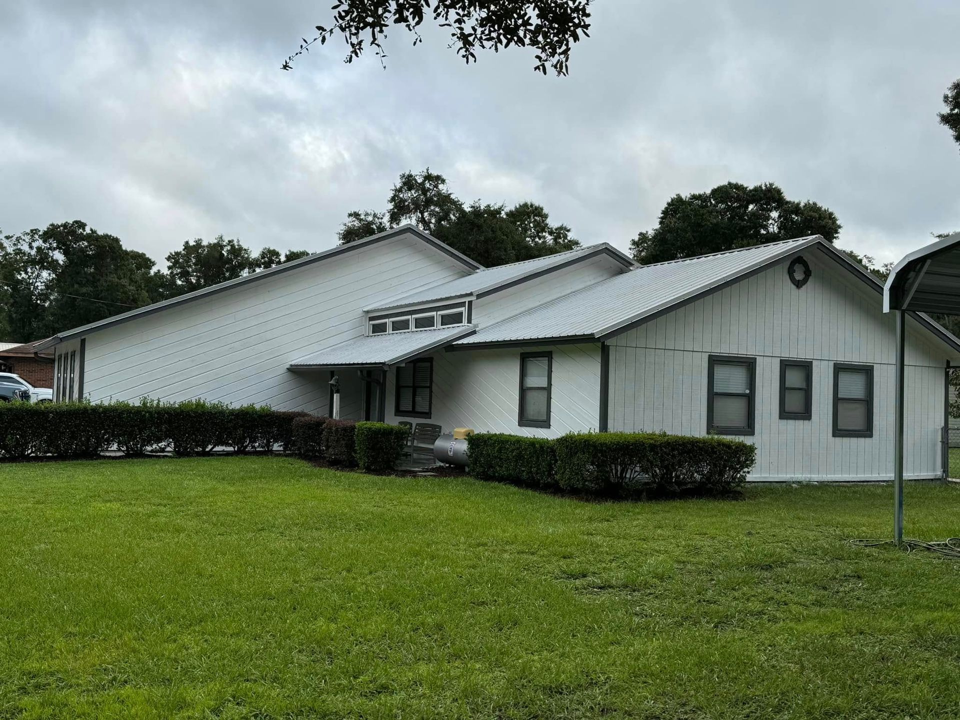 A white house with a metal roof is sitting on top of a lush green field.