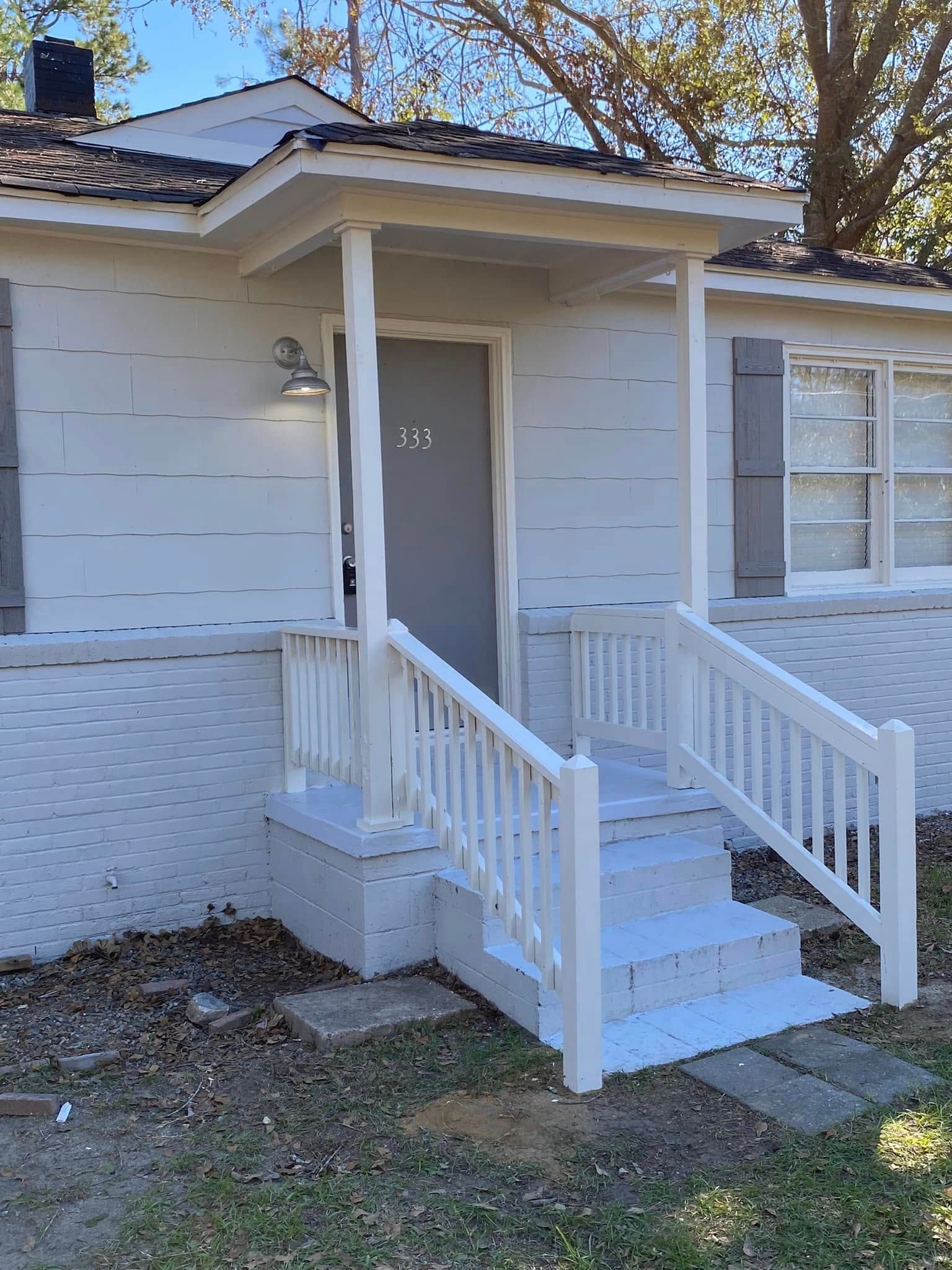 A white house with a porch and stairs in front of it.