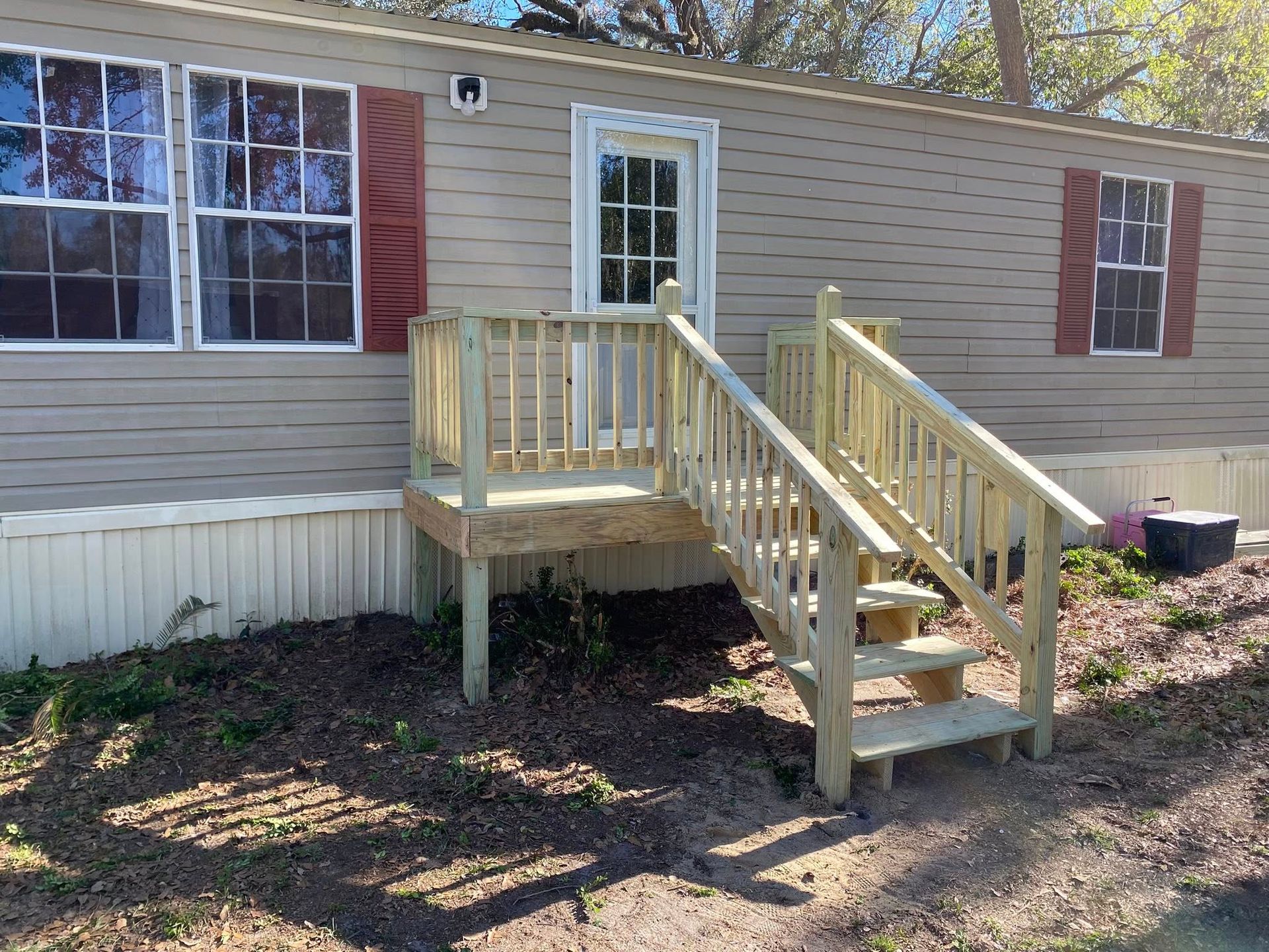 A mobile home with a wooden deck and stairs in front of it.