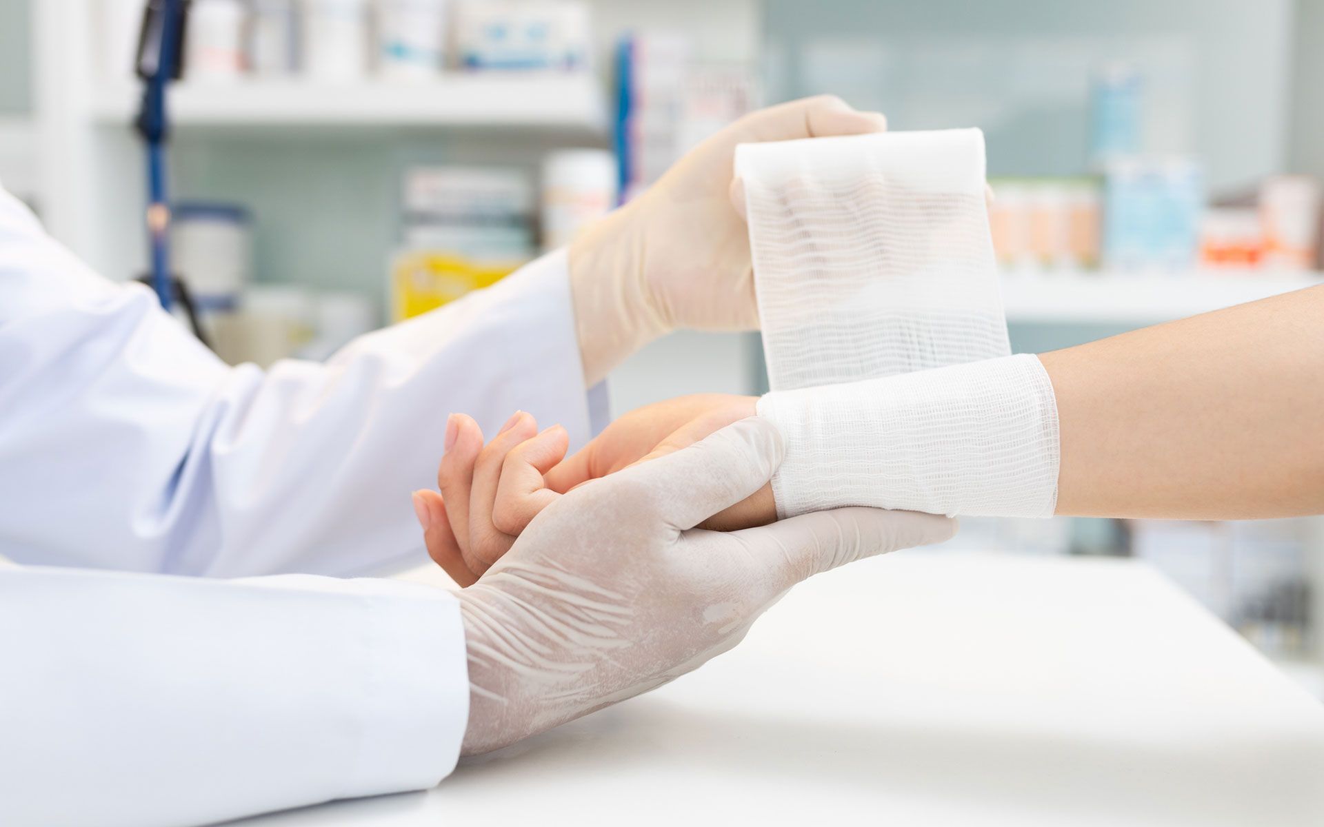 Doctor bandaging a patient's wrist with white gauze, in a clinic setting.