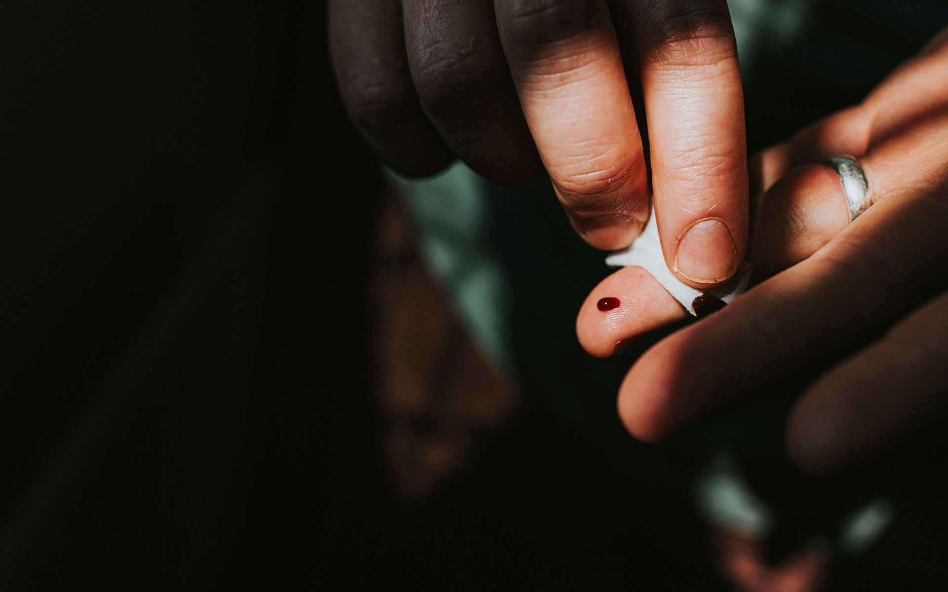A person cleaning a drop of blood from their finger with a cotton swab.