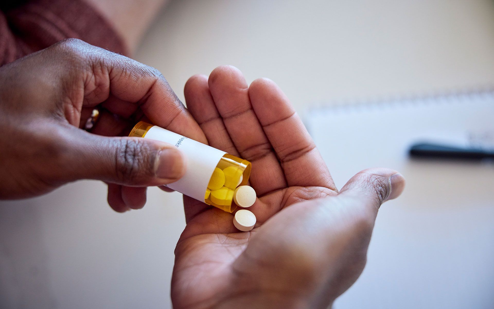 Hands holding a prescription pill bottle, pouring out two yellow pills.