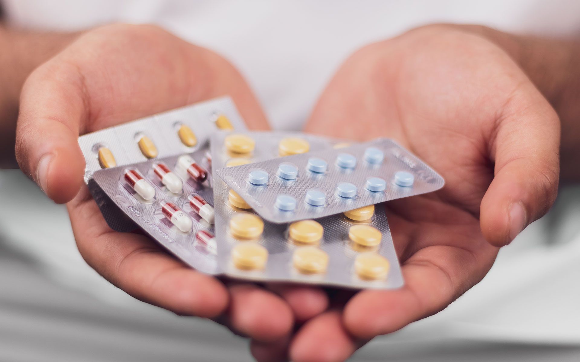 Person holding several blister packs of pills in their hands.