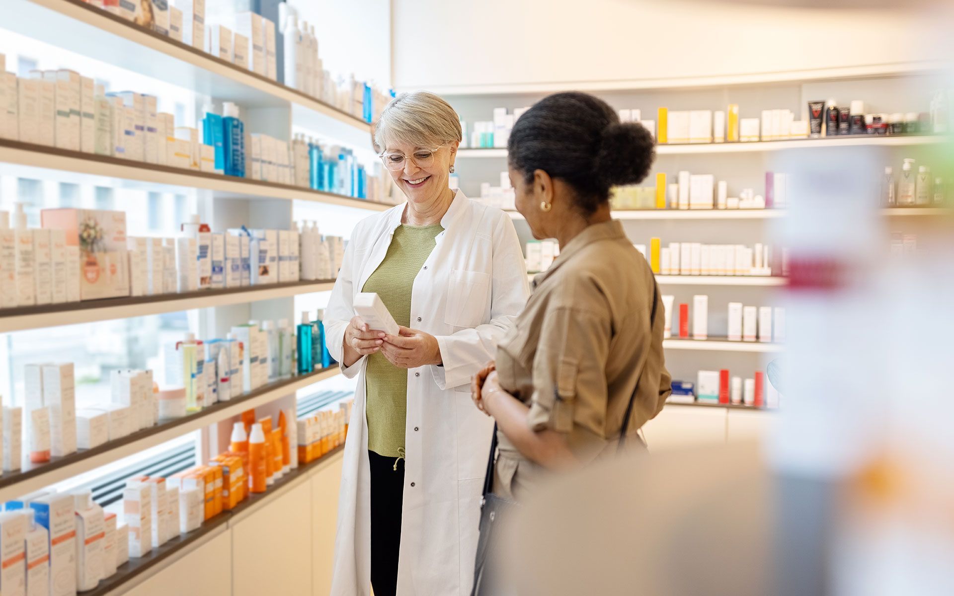 Pharmacist and customer in a brightly lit pharmacy, pharmacist shows product.