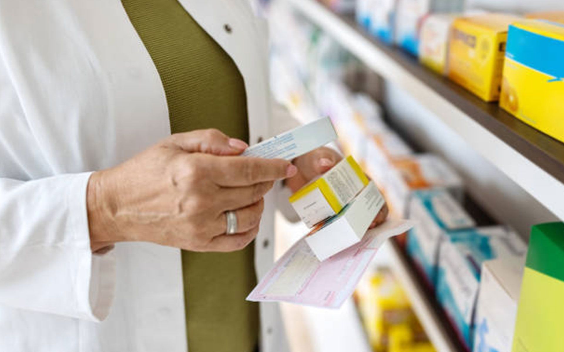Pharmacist in a white coat examines medication boxes, likely at a pharmacy.