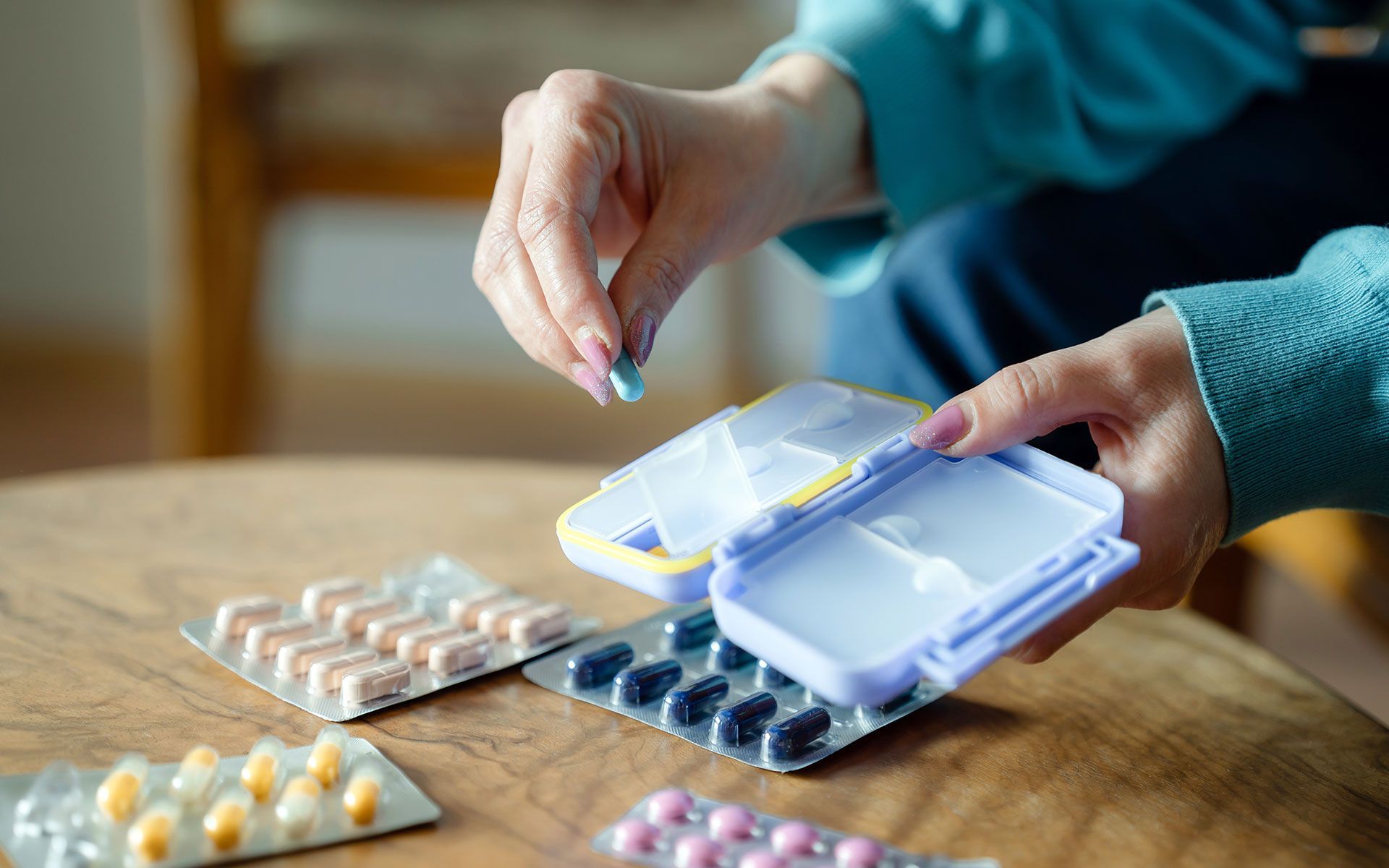 Person taking a pill from a pill organizer with blister packs on a table.