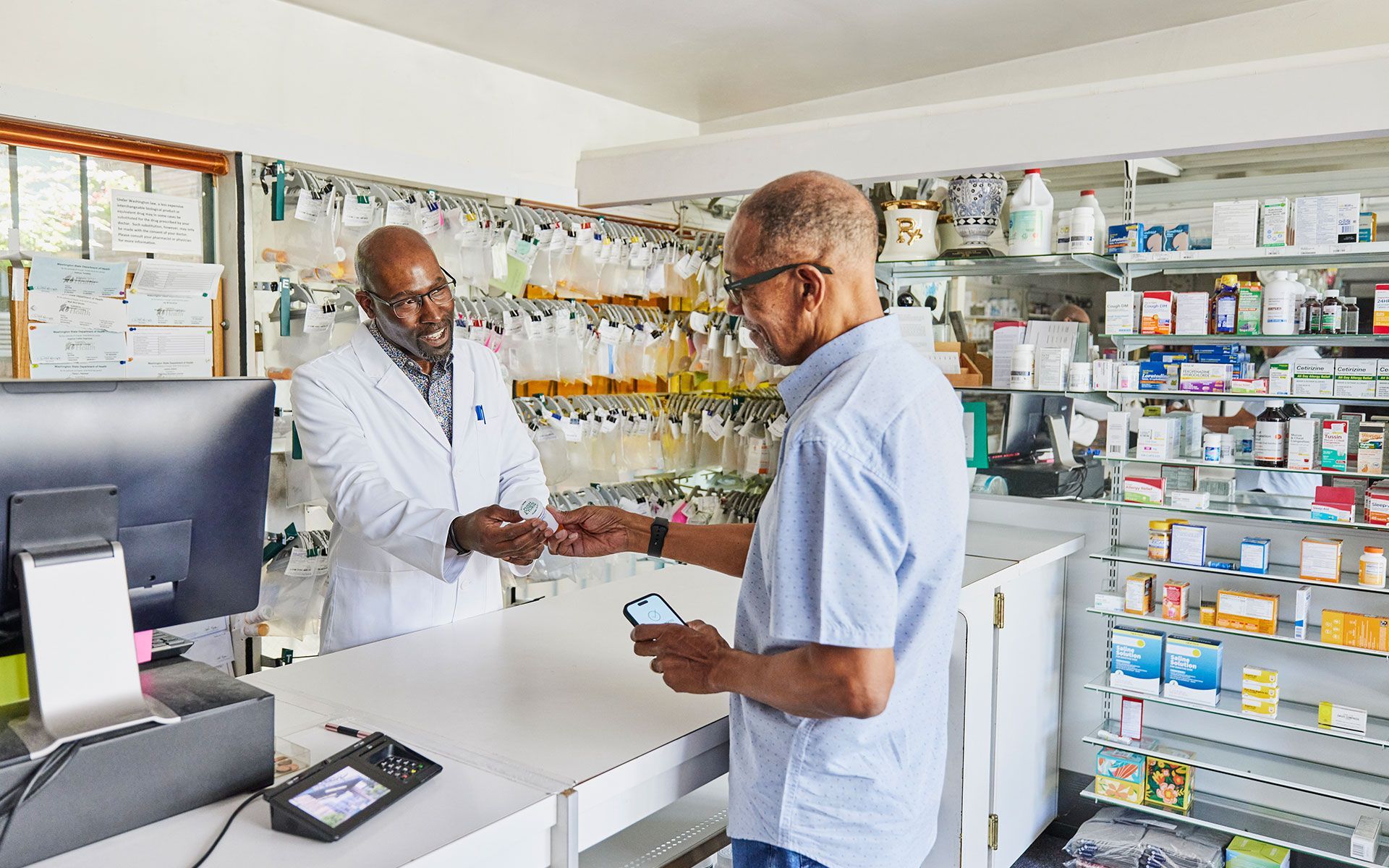 Pharmacist hands medication to customer at pharmacy counter. Shelves of products in background.