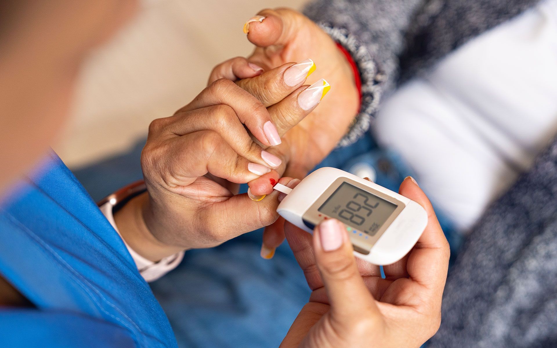 Person taking a blood sugar reading with a glucometer; a drop of blood on the fingertip.