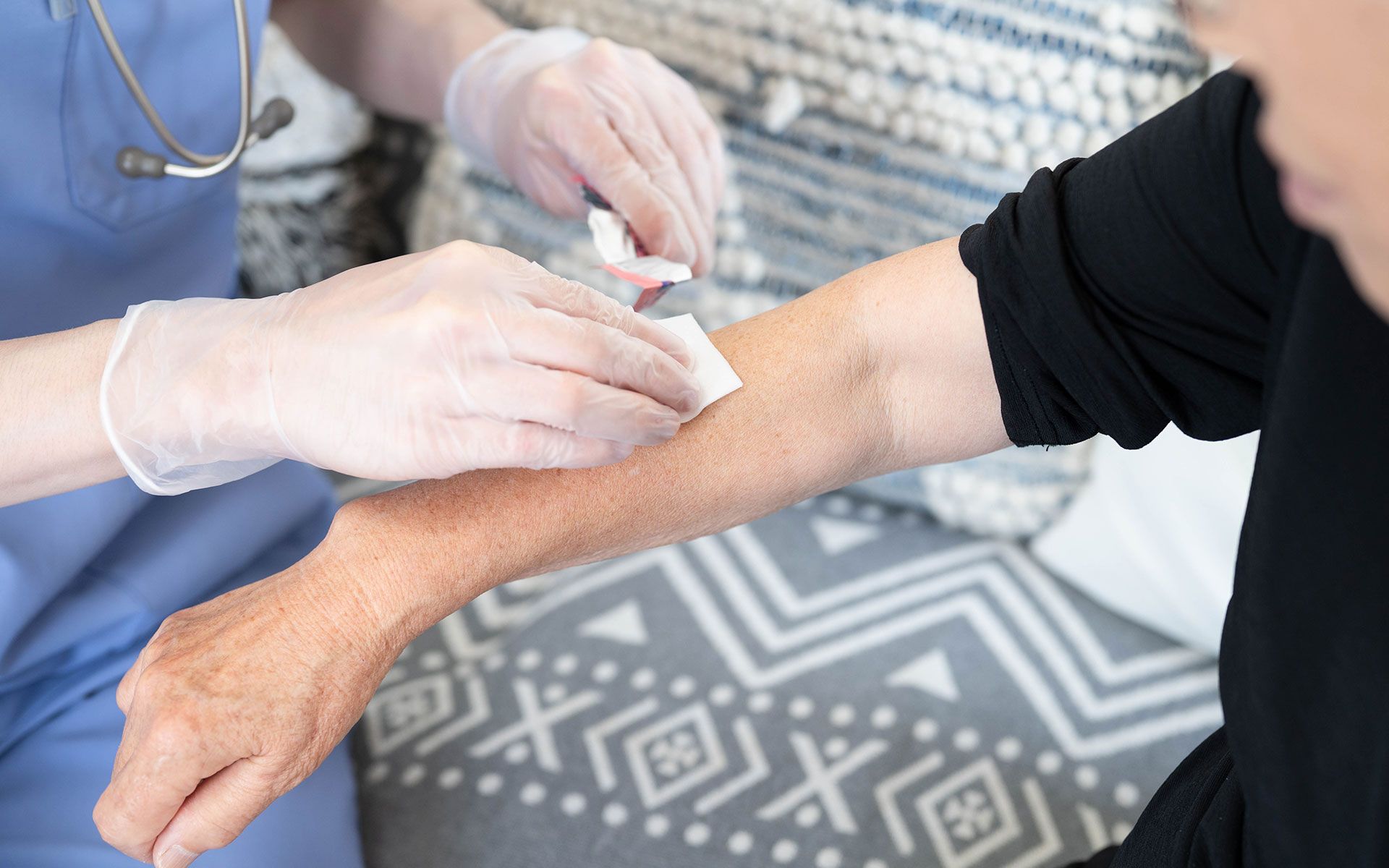 Nurse cleaning patient's arm with a swab; patient in black shirt and nurse in blue scrubs.