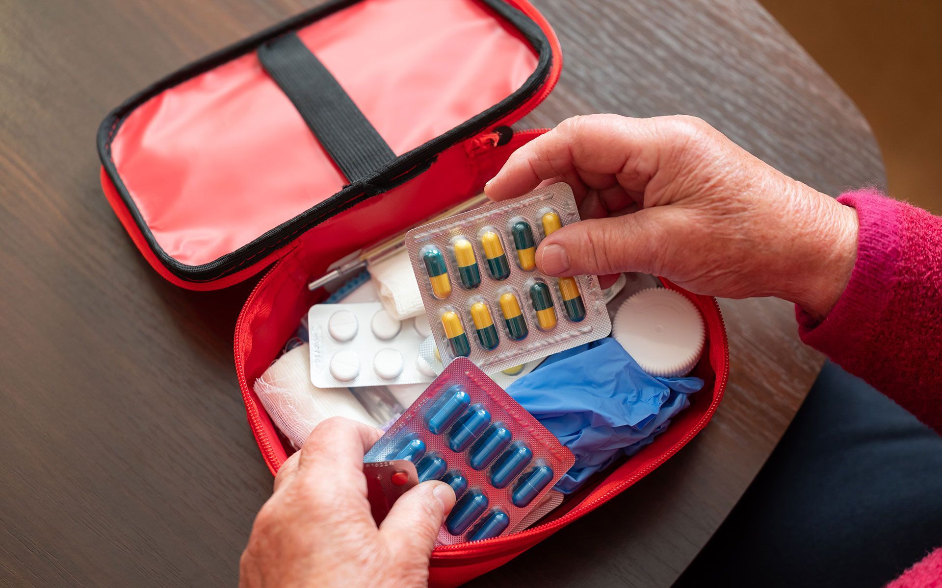 Hands holding medications in a red first aid kit.