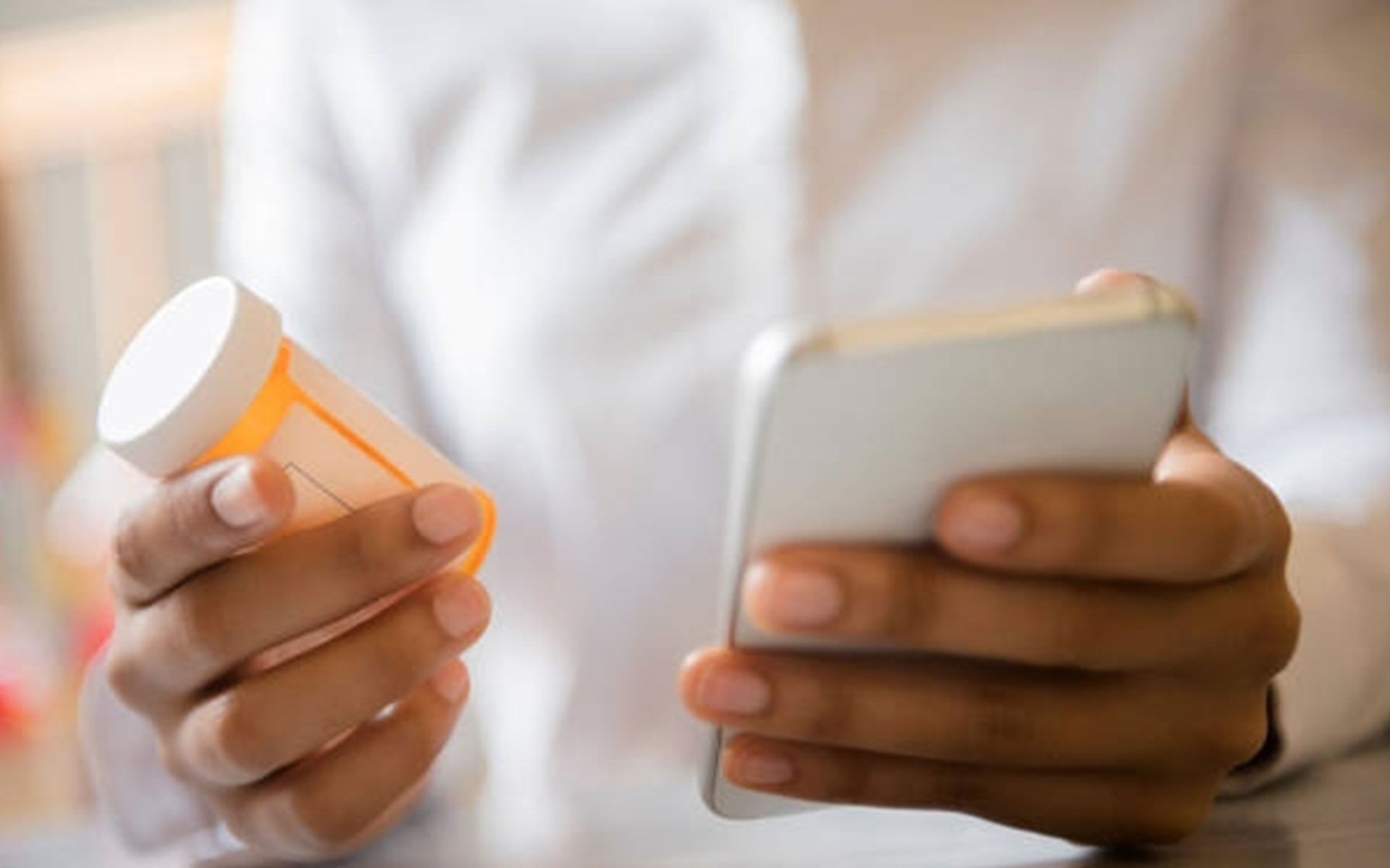 Person holding prescription bottle and smartphone.