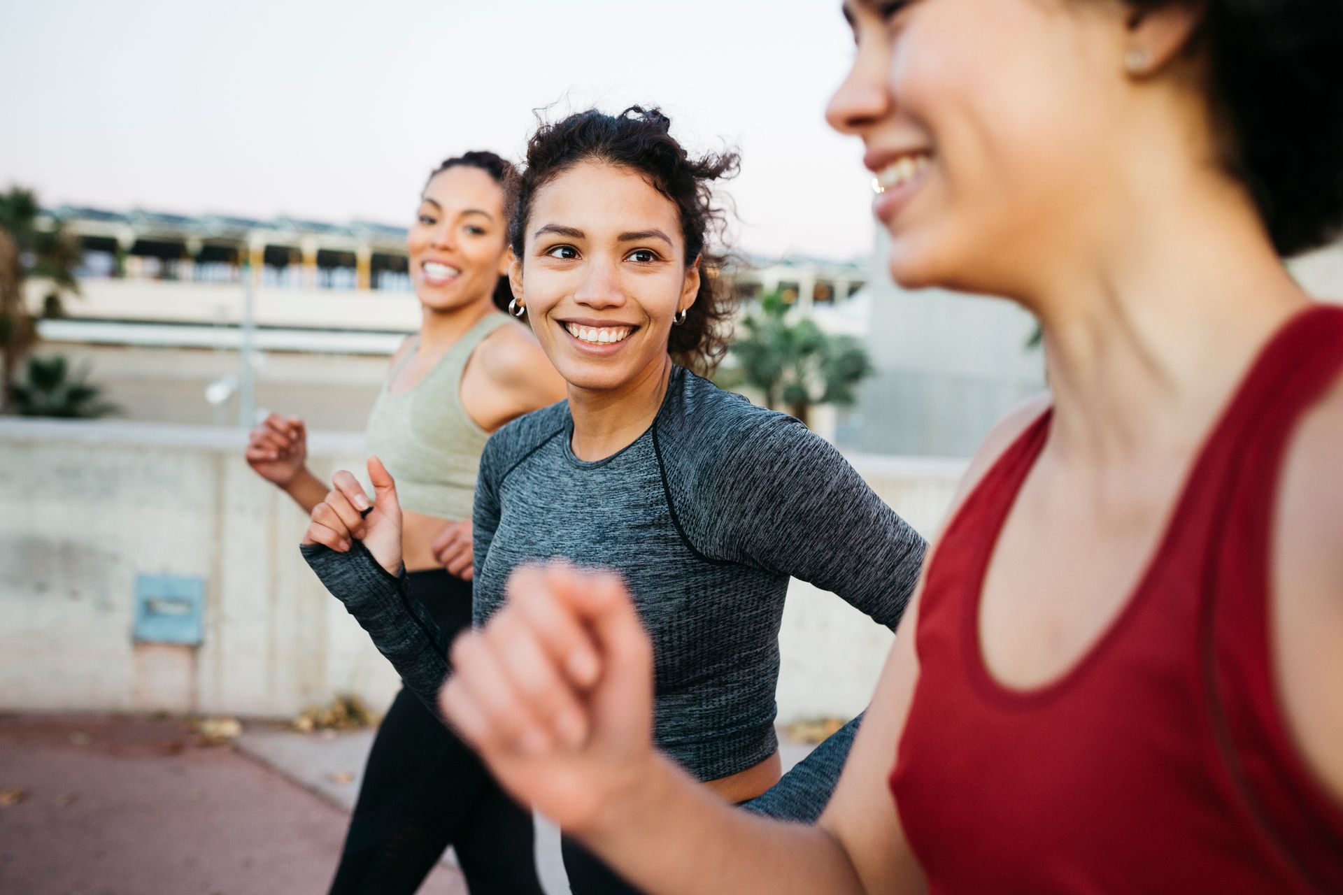 Three smiling women running together outdoors.