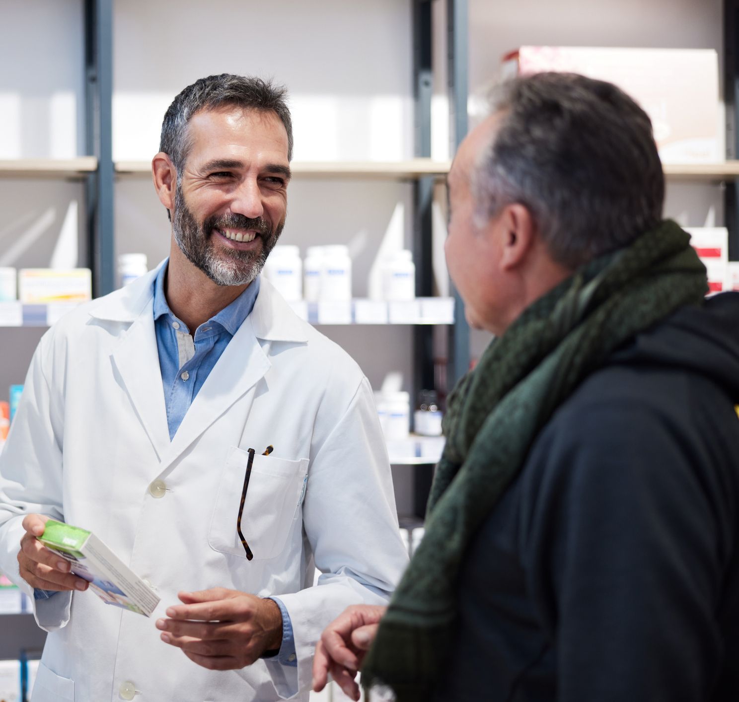 Pharmacist in white coat smiles, explaining medication to customer in pharmacy.