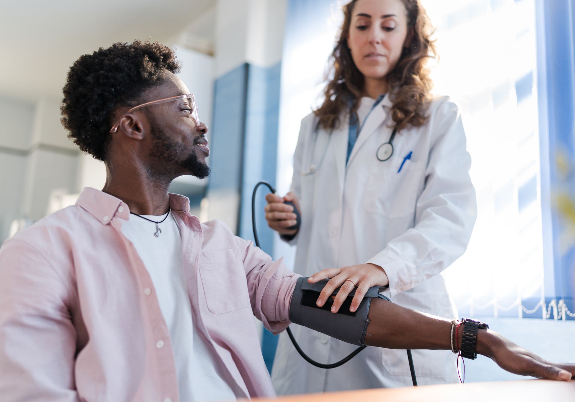 A doctor taking a Black man's blood pressure in a doctor's office.
