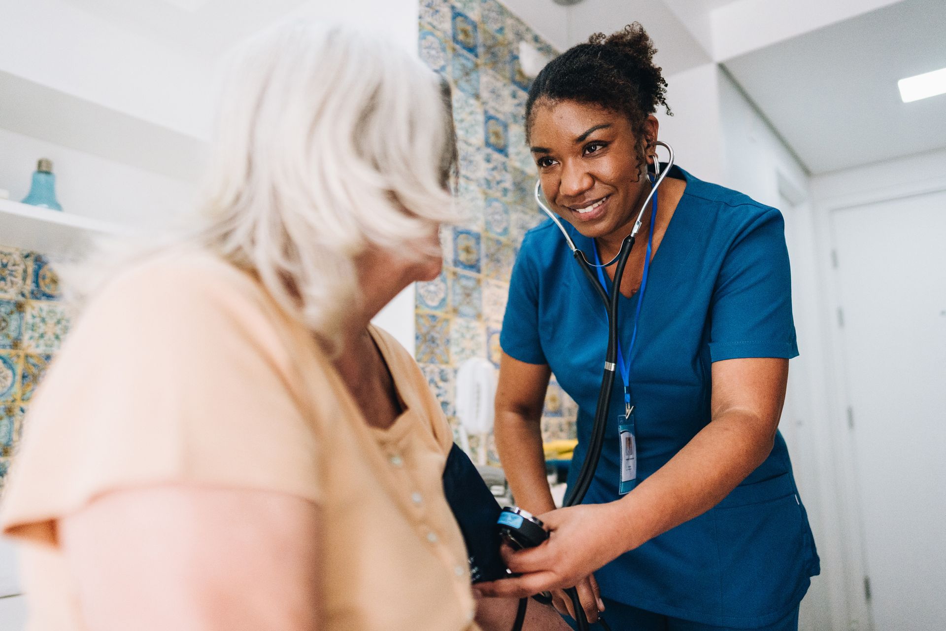 Nurse taking elderly patient's blood pressure in a room, smiling.