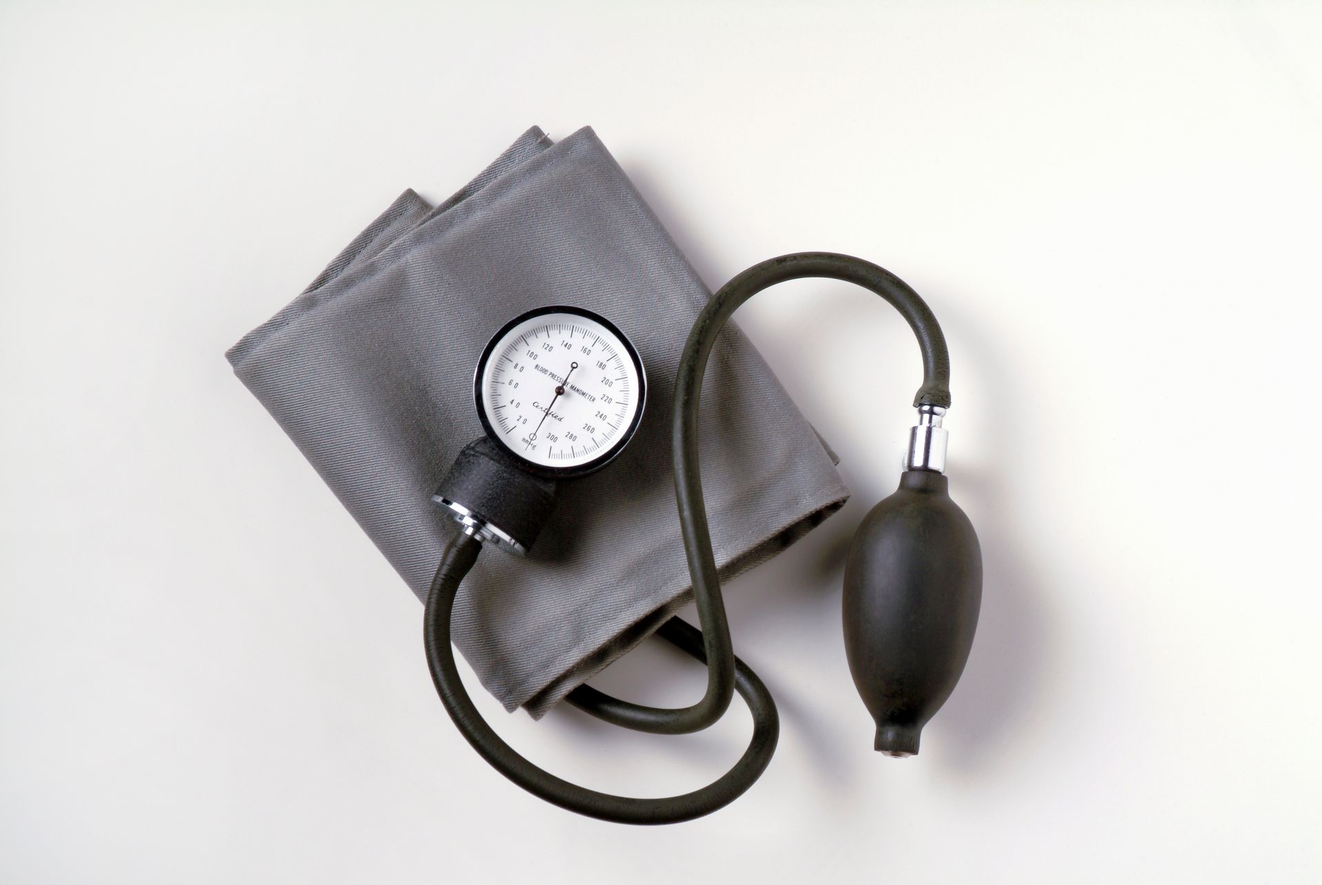 Blood pressure cuff on white background. Gray arm cuff, black gauge, and inflation bulb.
