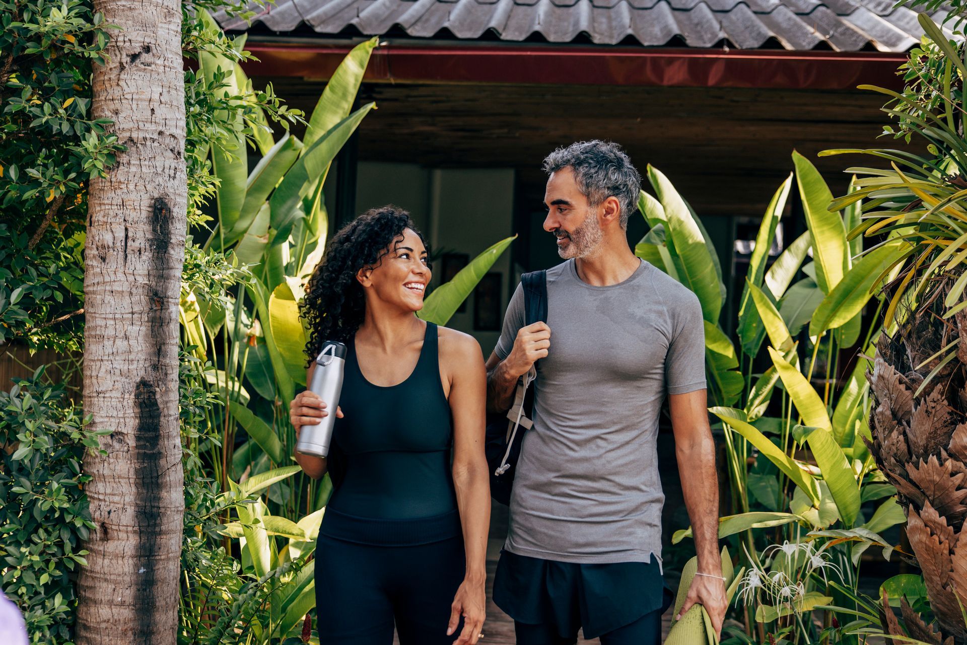 Smiling couple in athletic wear, walking outdoors, surrounded by greenery.