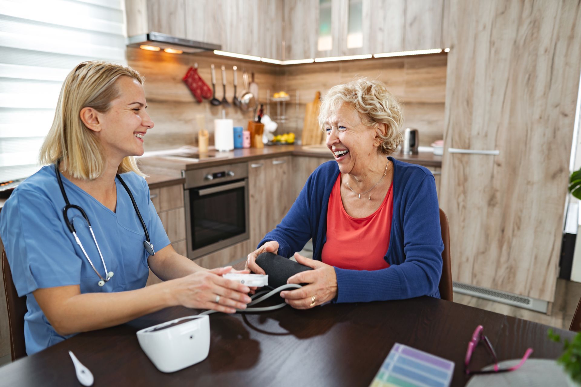 Nurse taking elderly woman's blood pressure in a kitchen. Both women are smiling.