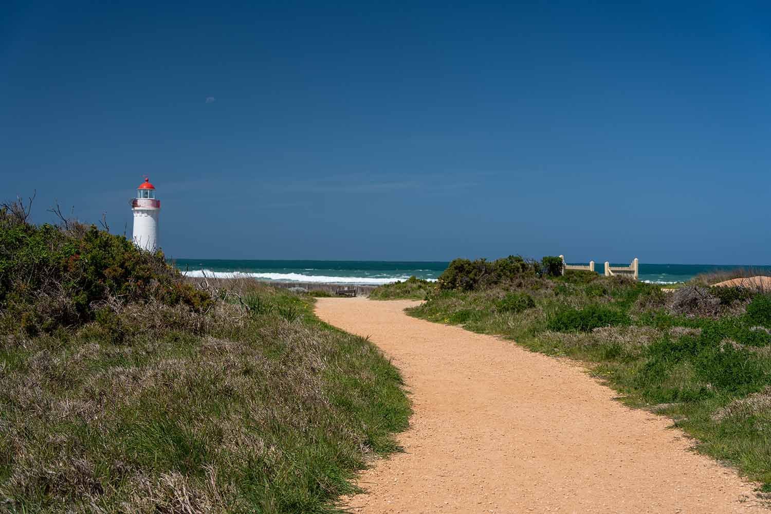 A Dirt Path Leading To A Lighthouse On The Beach — Warrnambool Emergency Plumbing in Warrnambool, VIC