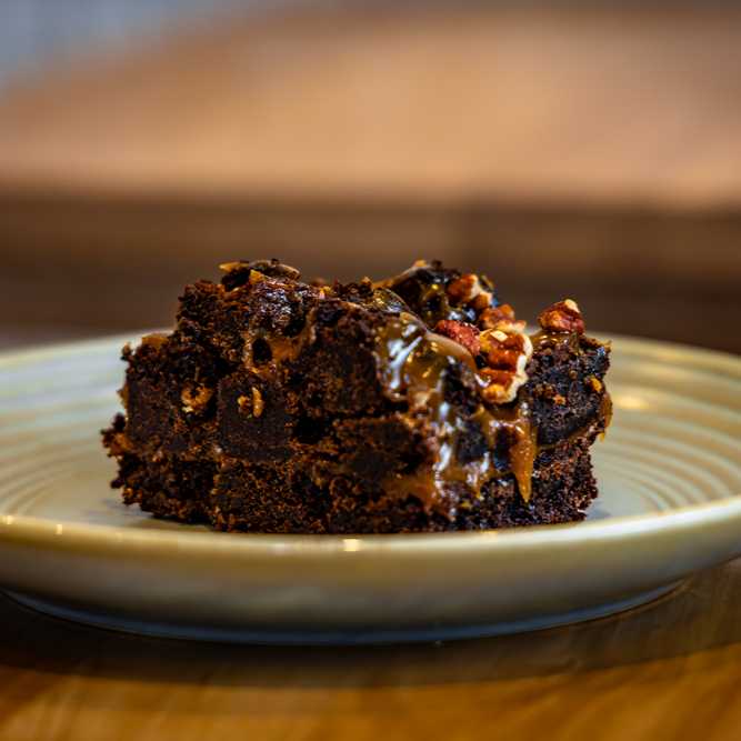 Chocolate brownie with caramel and pecans on a plate.