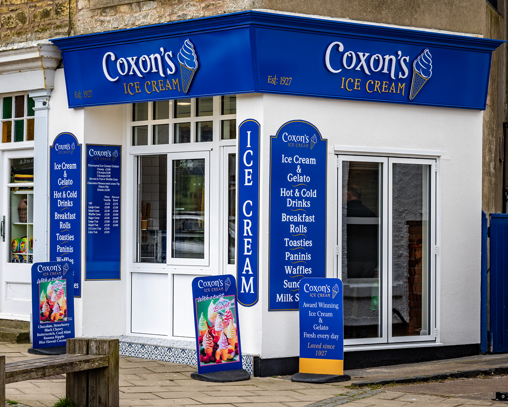 Coxon's Ice Cream shop with blue and white signage. Offers ice cream, breakfast items, and drinks.