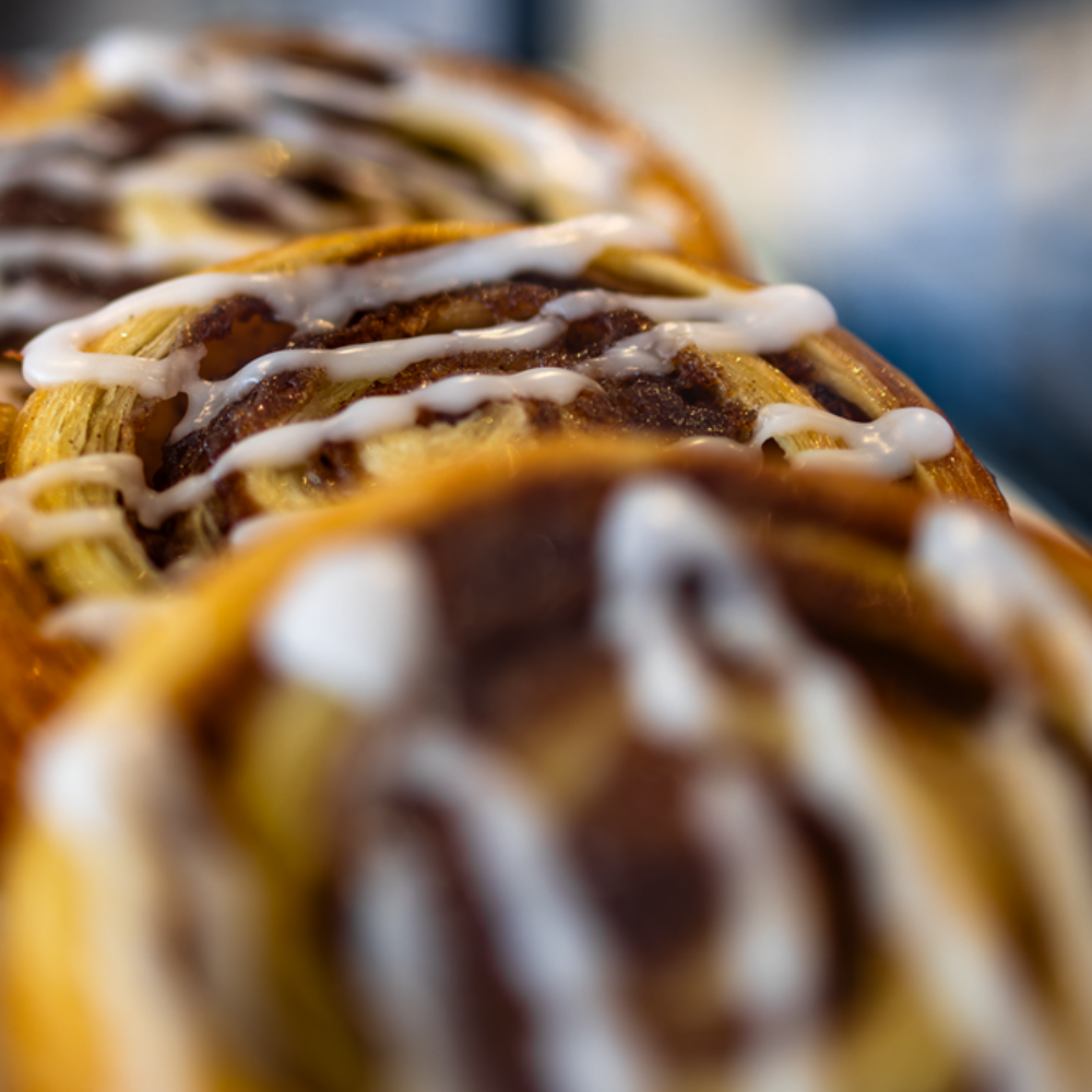 Close-up of glazed cinnamon rolls, brown filling, white icing drizzled on top.