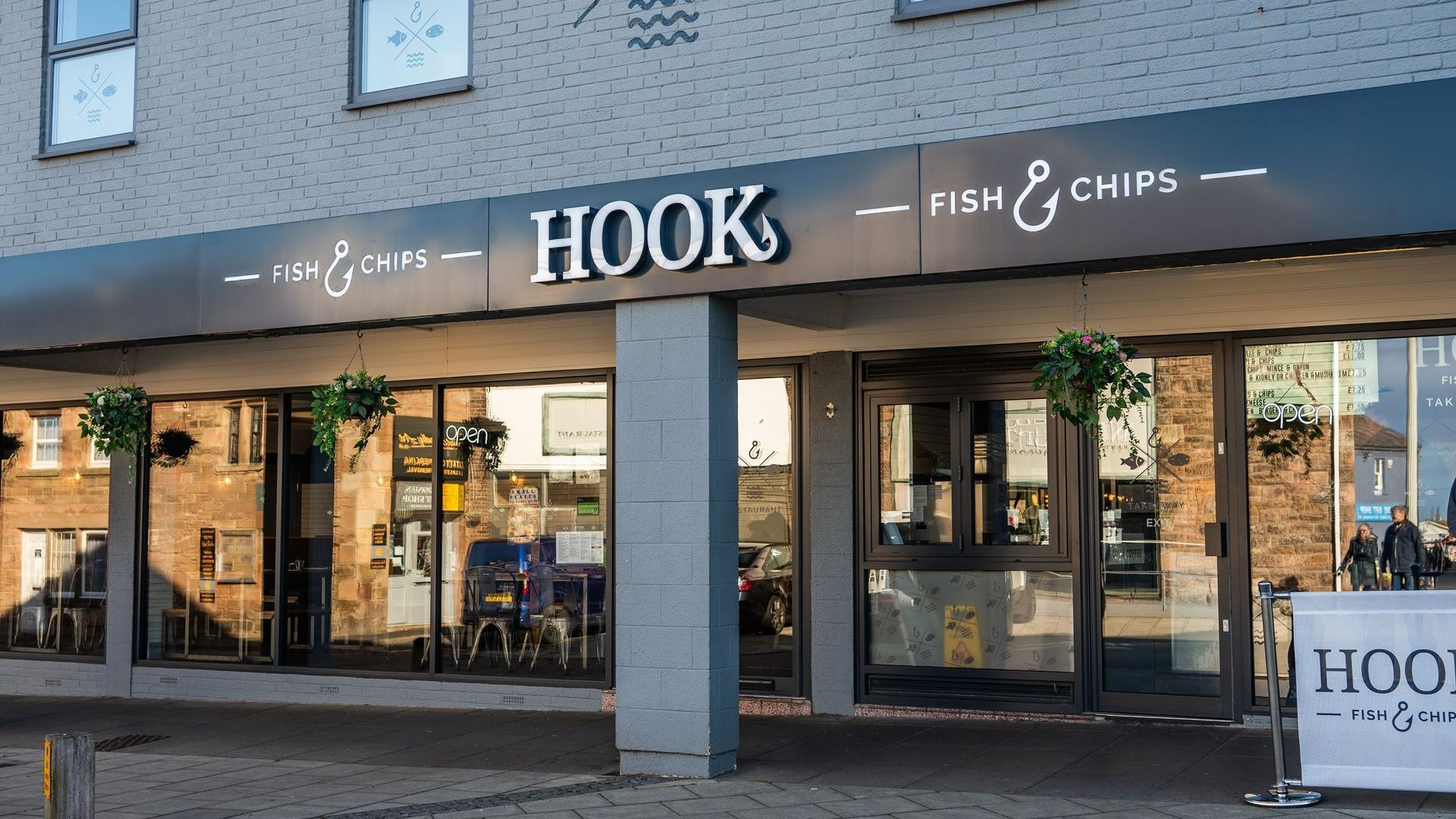A hook fish and chips restaurant with a hanging basket of flowers