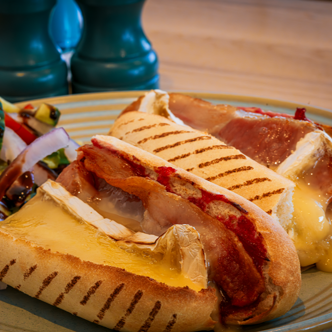 Grilled sandwich with melted cheese, prosciutto, and side salad on a plate.