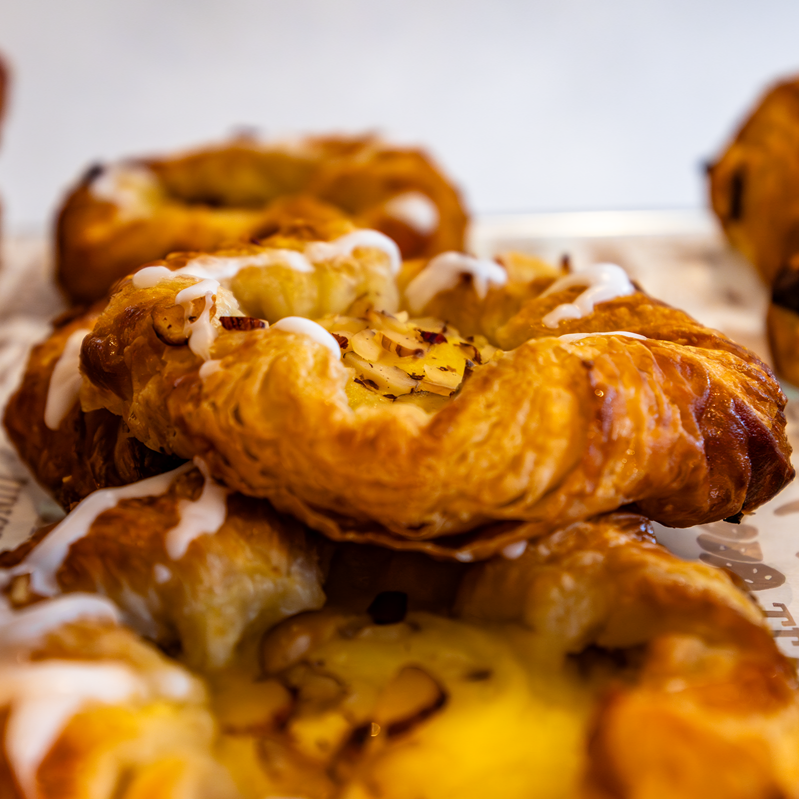 Golden-brown pastries with almond slices and white icing in a bakery display.