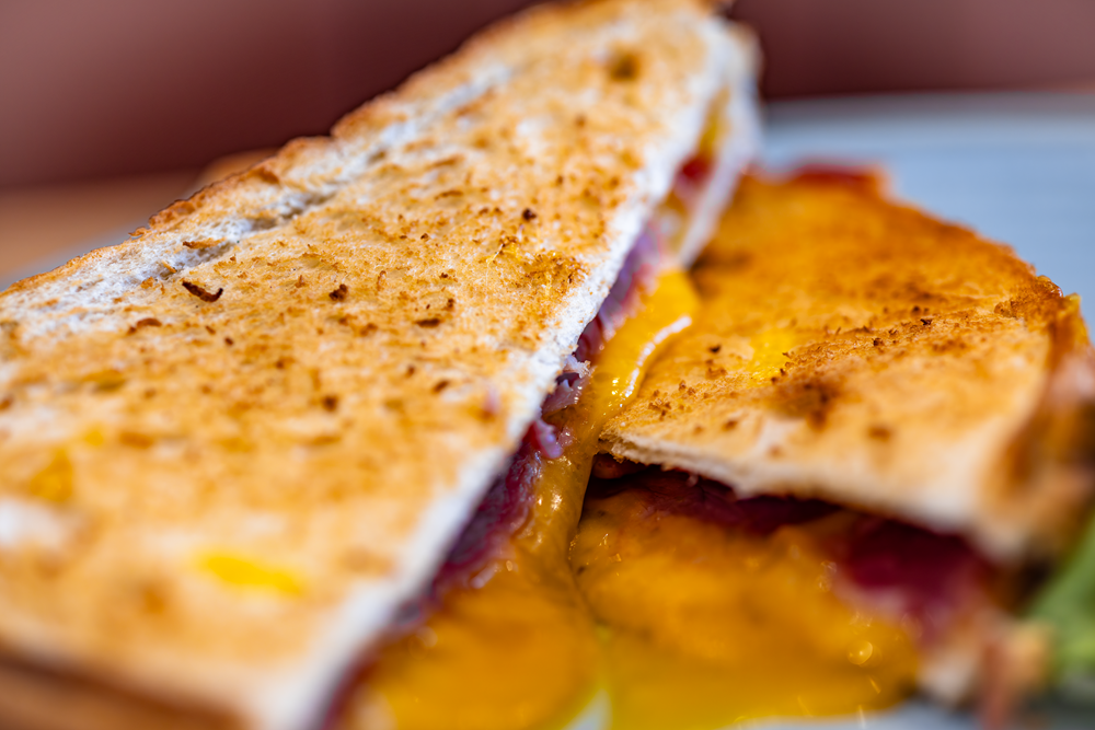 Grilled cheese sandwich cut in half, cheese melting, toasted bread.
