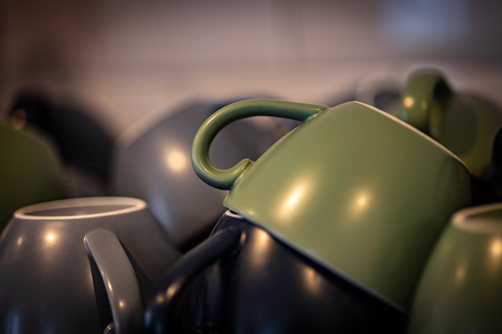 Stack of gray and green coffee cups with curved handles.