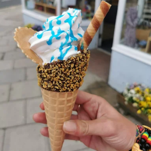 Hand holding ice cream cone with blue drizzle, wafer, and chocolate-covered nuts.