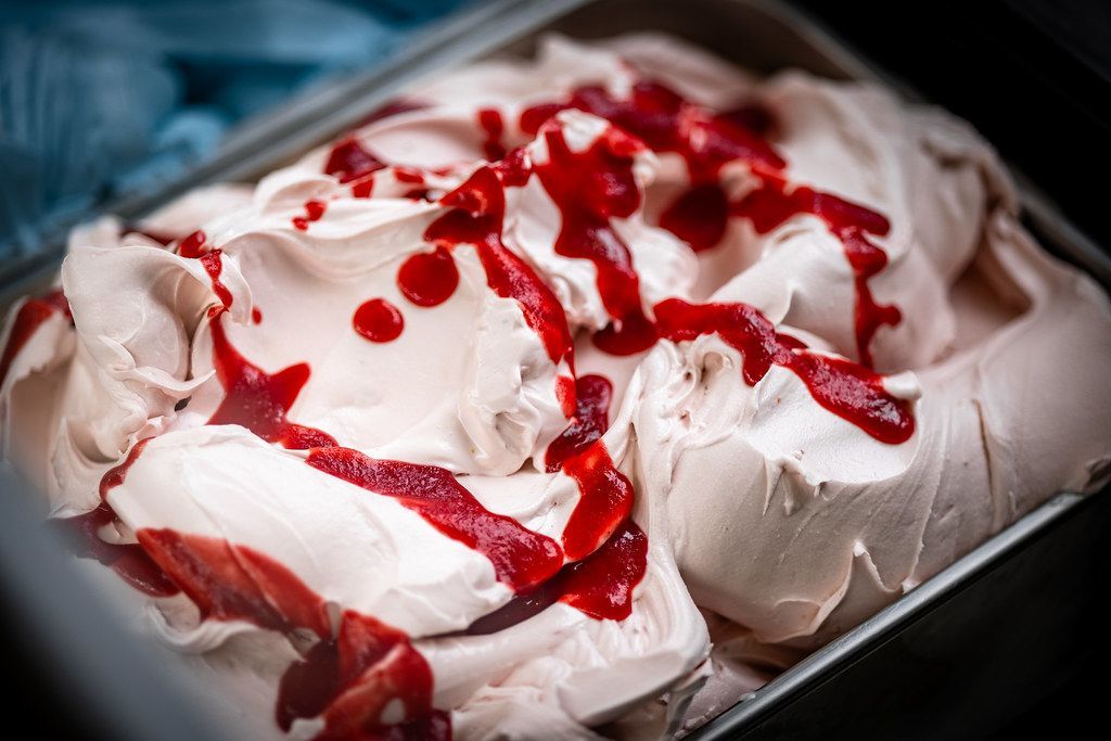 Ice cream with red sauce drizzled on top in a metal container.