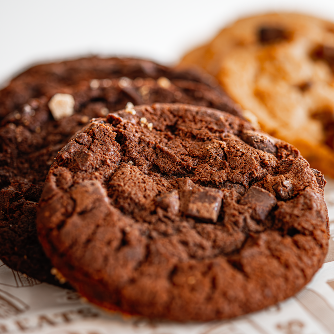 Close-up of chocolate cookies with chunks of chocolate on a patterned surface.