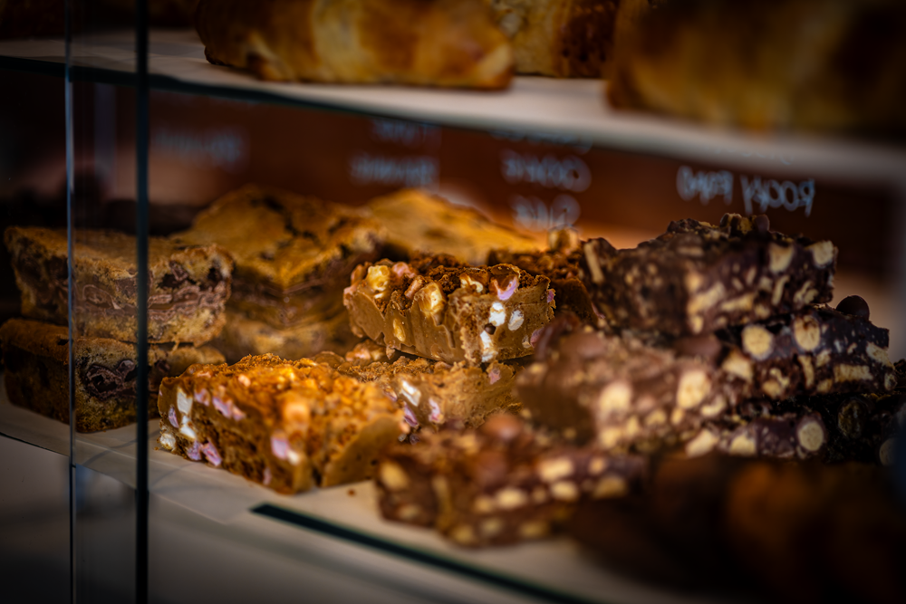 Close-up of a bakery display case with various baked treats: brownies, fudge, and other desserts.
