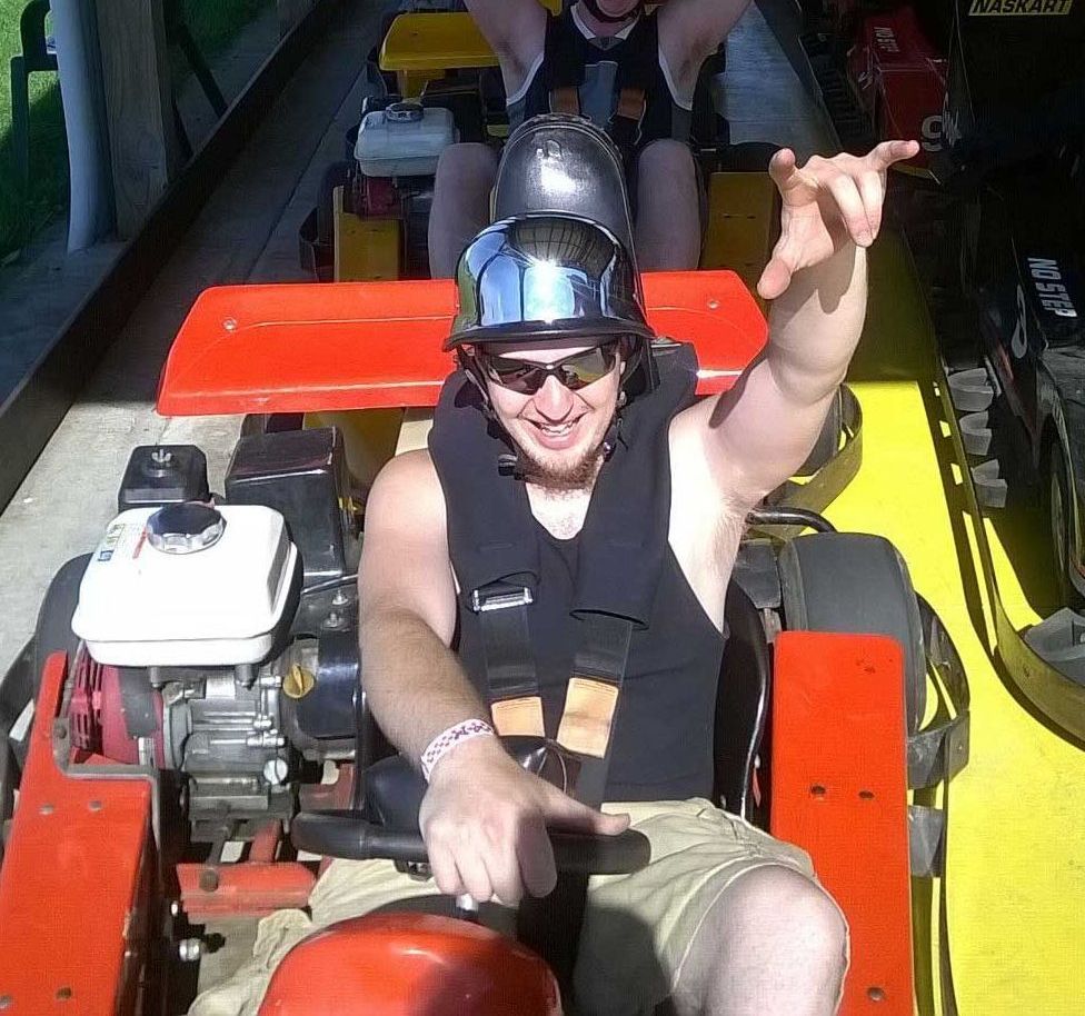 A man wearing a helmet and sunglasses is sitting in a red and yellow vehicle - Orville, OH - Putt-N-Stuff