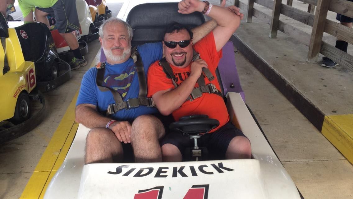Two men are sitting in a sidekick go kart.