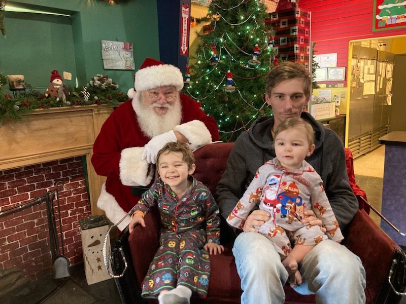 A man and two children are sitting in a chair with santa claus.