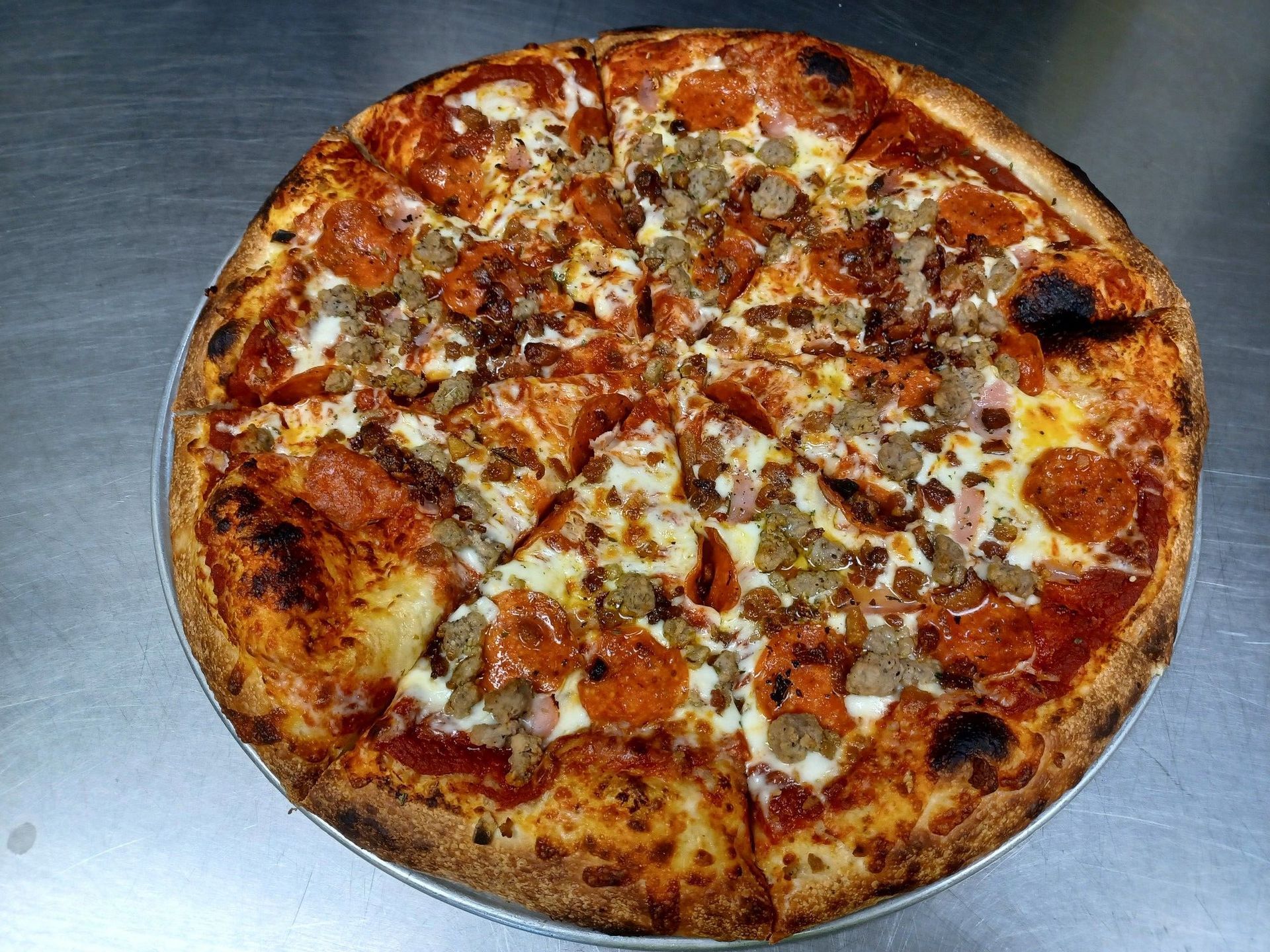 A pizza with pepperoni , sausage , and cheese is on a pan on a table.