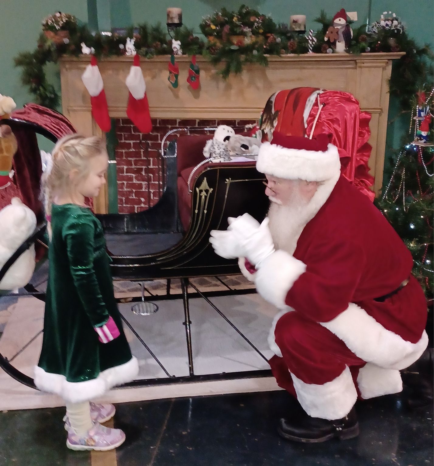 A little girl in a green dress talks to santa claus