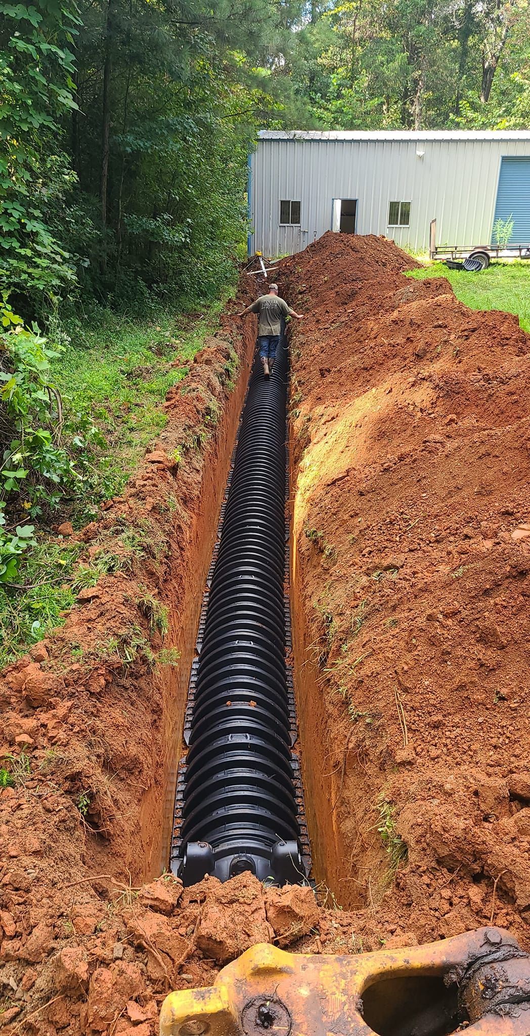 A man is standing in a trench next to a large pile of dirt.